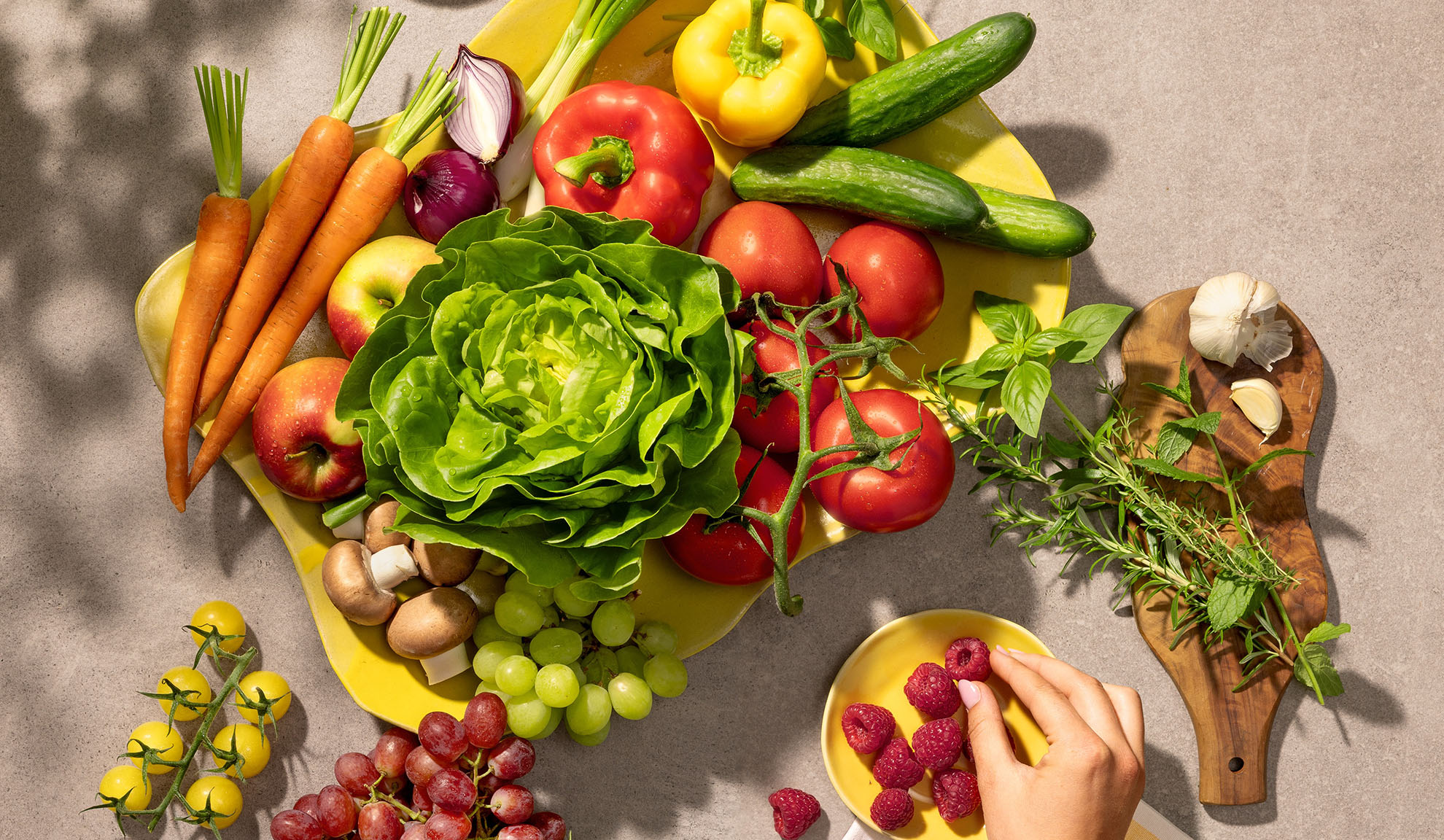 Légumes et fruits frais sur un plat jaune, incluant carottes, laitue, poivrons, tomates et raisins.