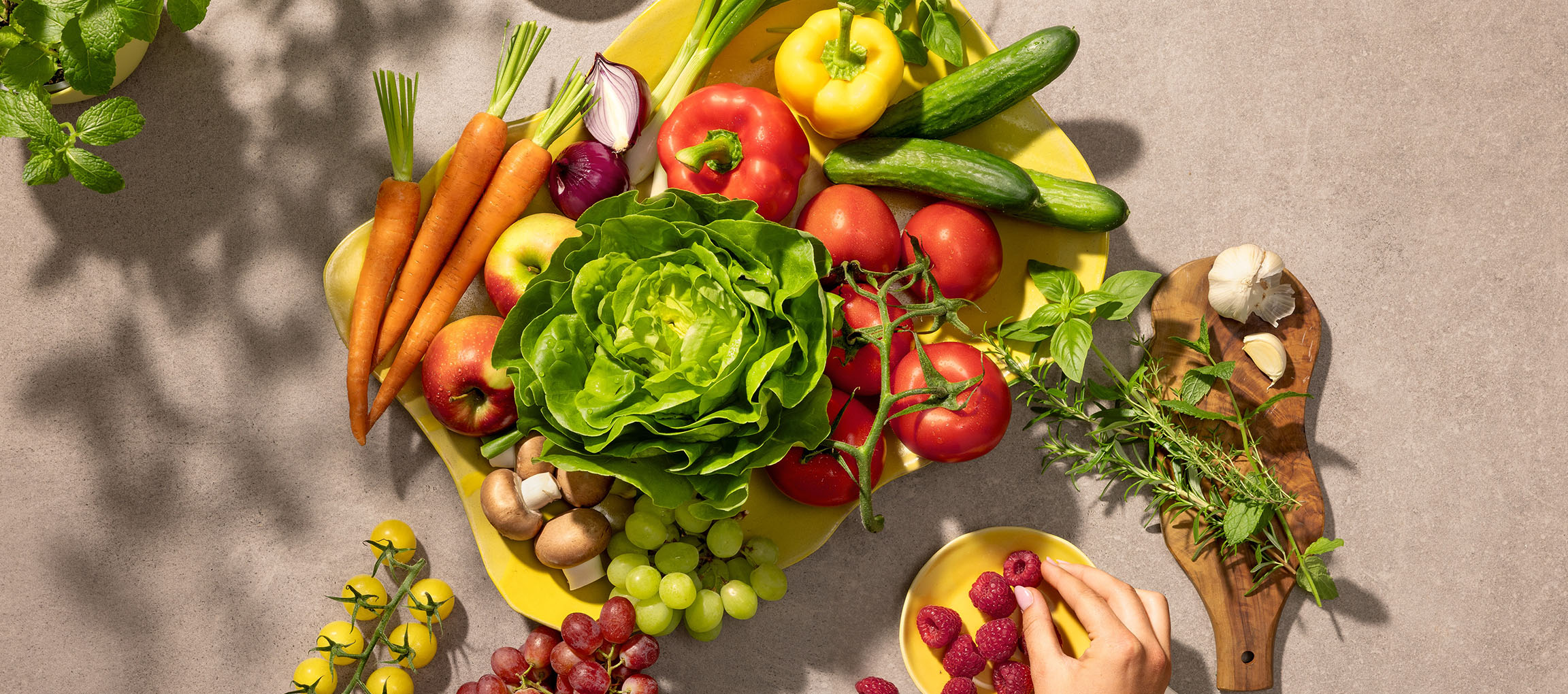 Légumes et fruits frais sur un plat jaune, incluant laitue, tomates, carottes et baies.