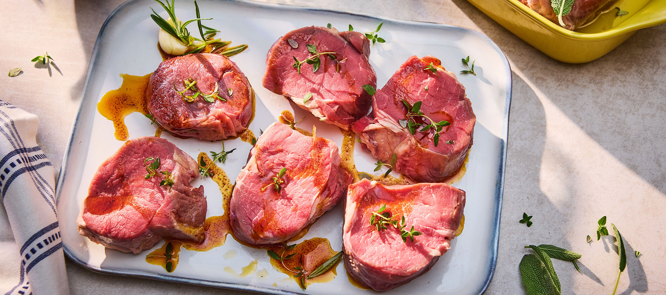 Steaks de bœuf frais avec herbes et huile sur un plat blanc.