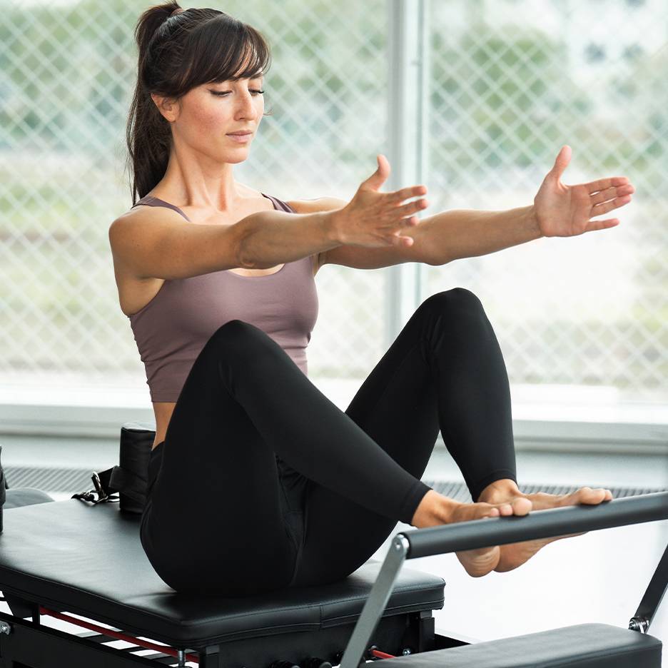 Femme faisant du Pilates sur un reformer, portant un haut et un legging noir.