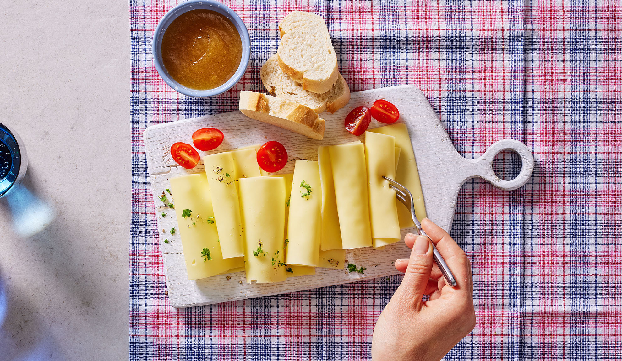 Tranches de fromage, tomates cerises, pain et confiture sur une planche à servir.
