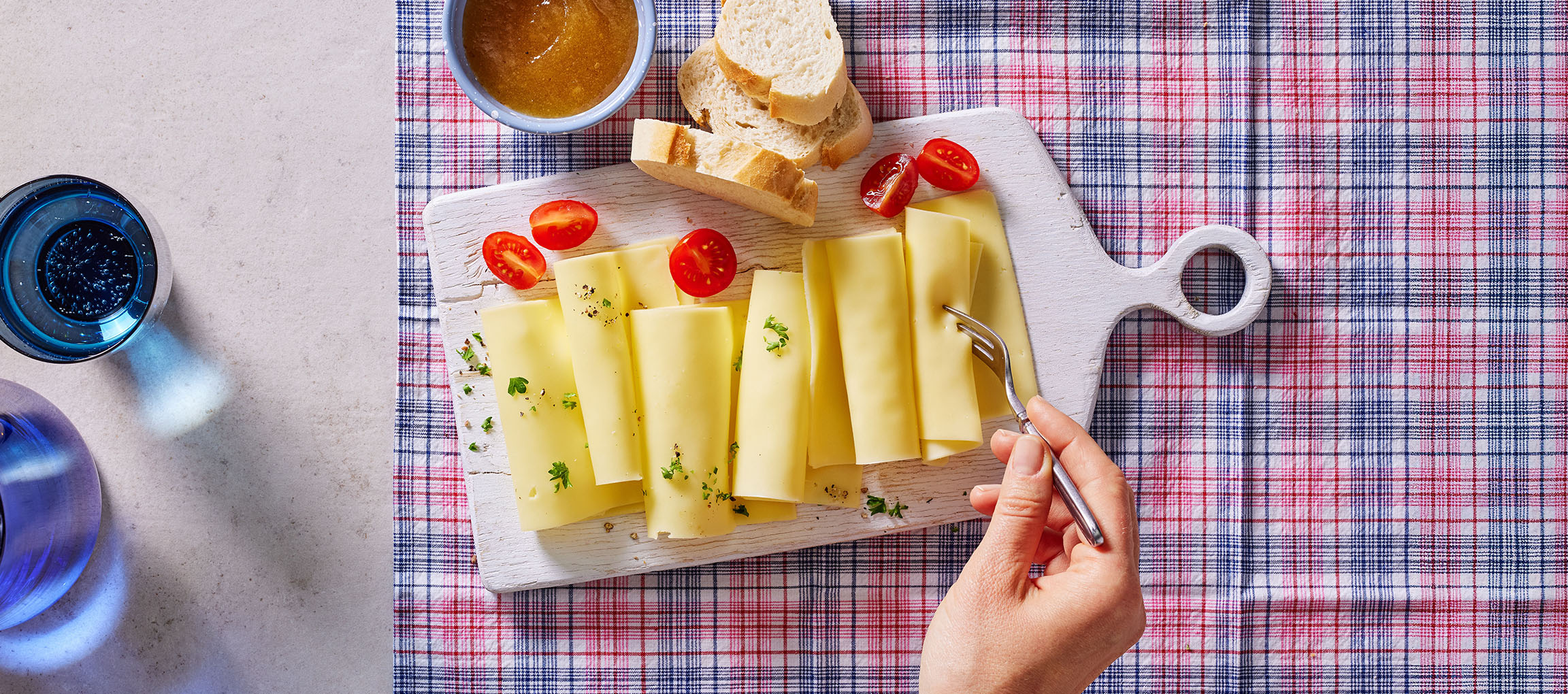 Tranches de fromage avec tomates cerises, pain et confiture sur une nappe à carreaux.