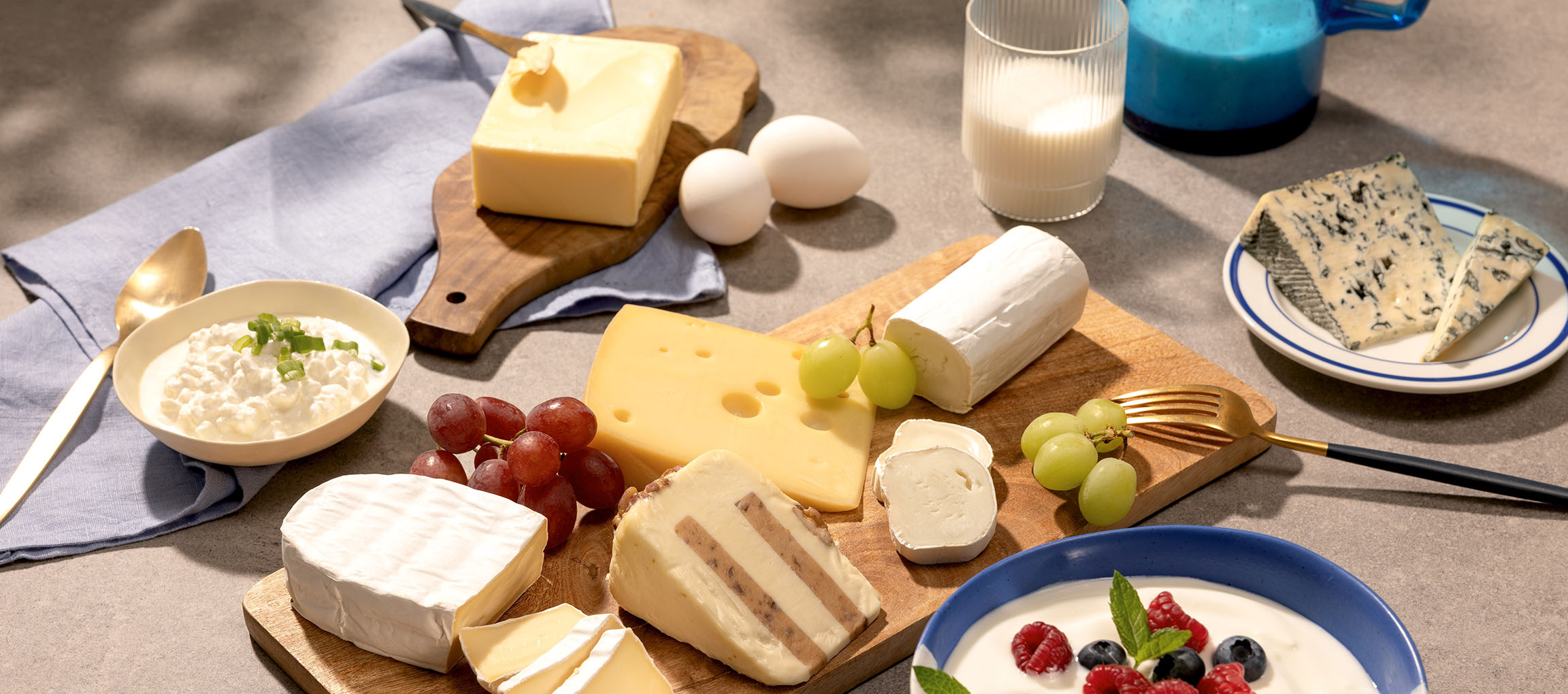 Assortiment de fromages, œufs, raisins, lait et yaourt aux baies sur une table.
