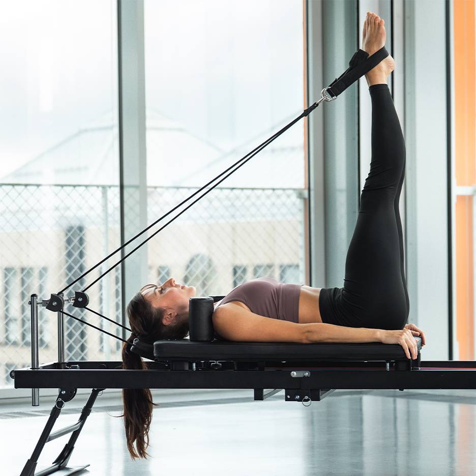 Femme faisant un exercice de jambes sur un appareil de Pilates reformer.