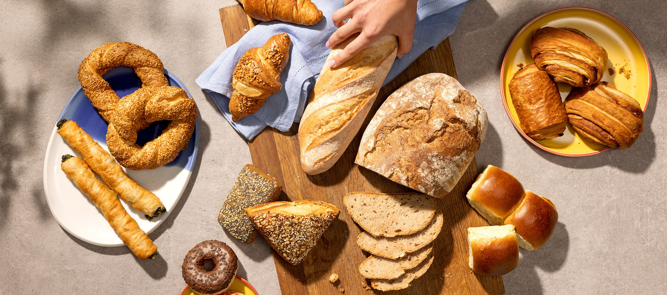Assortiment de pâtisseries et de pains, incluant bretzels, croissants et baguettes, sur une table.