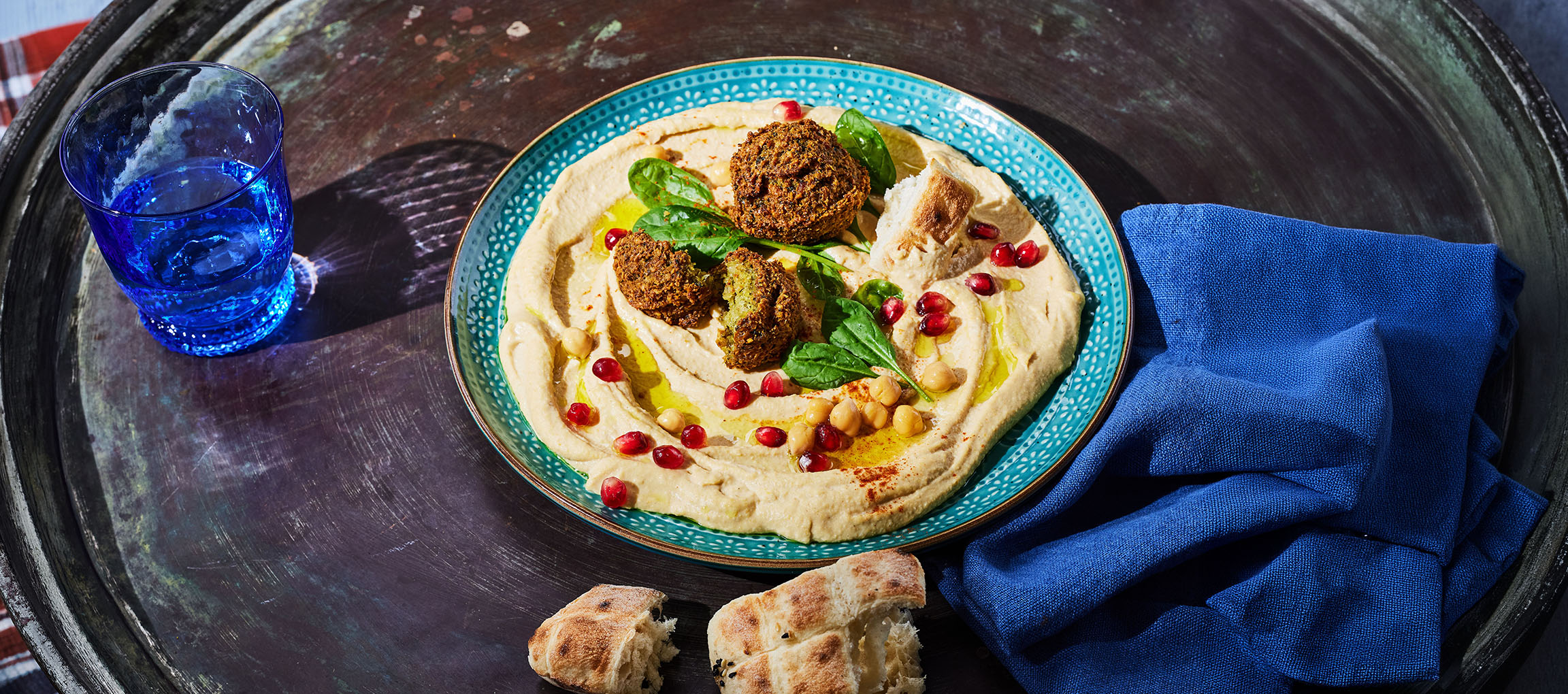 Houmous avec falafels, graines de grenade et pain sur un plateau métallique.