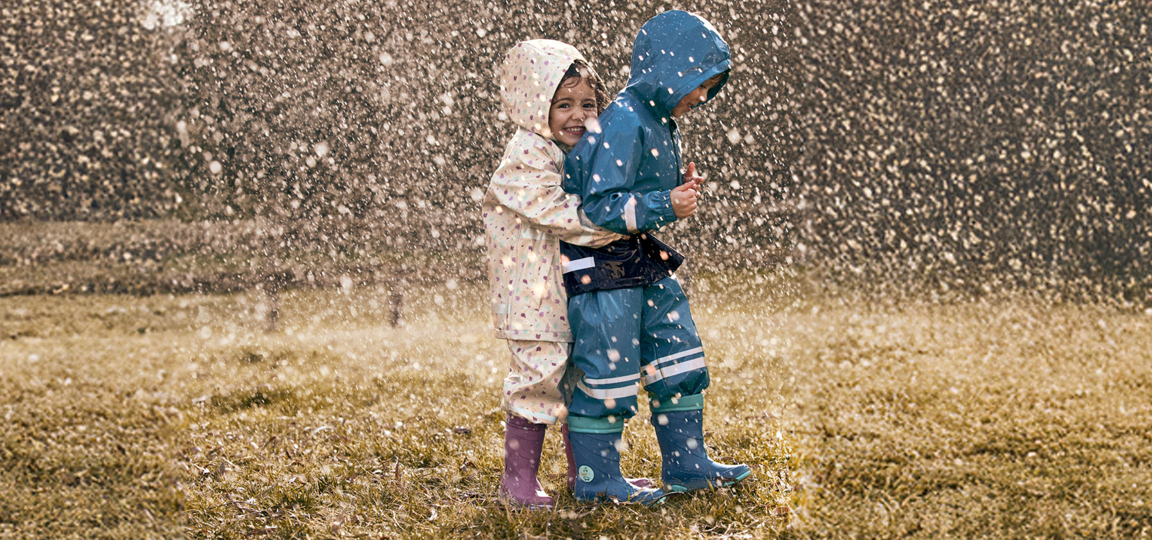Deux enfants en cirés et bottes de pluie jouent sous la pluie.