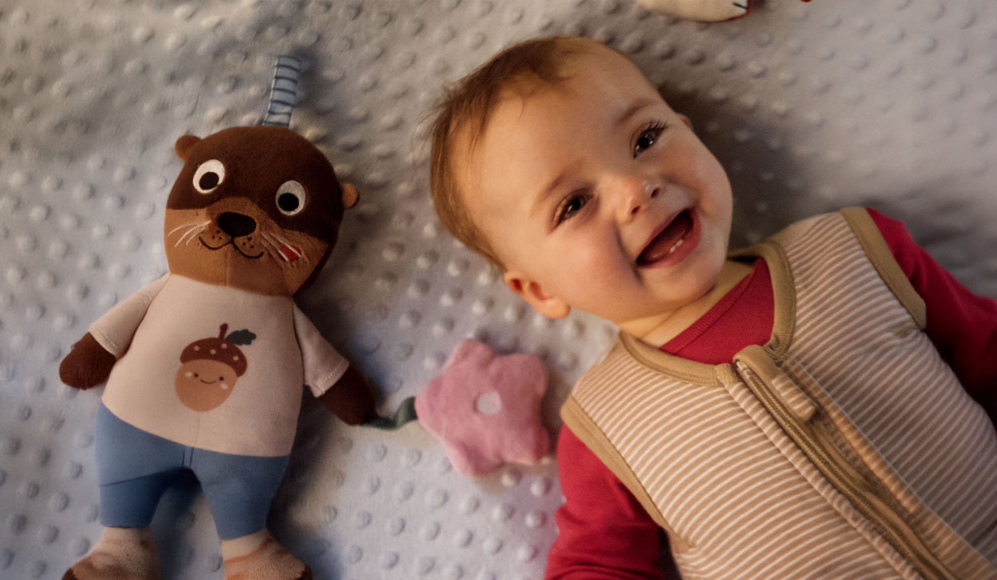 Un bébé souriant et une peluche de loutre sur une couverture douce.