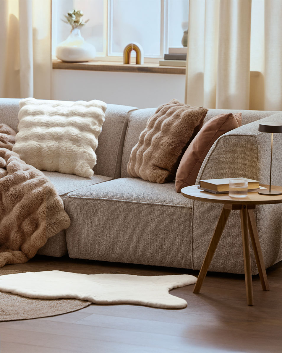 Canapé modulaire gris avec coussins et plaids moelleux, table d'appoint en bois.