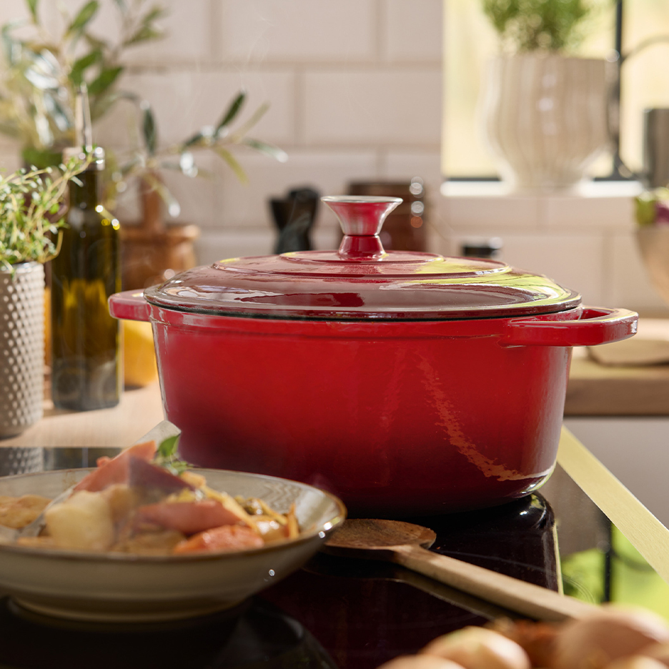 Une cocotte en fonte rouge sur une plaque de cuisson, avec un bol de plat cuisiné à côté.