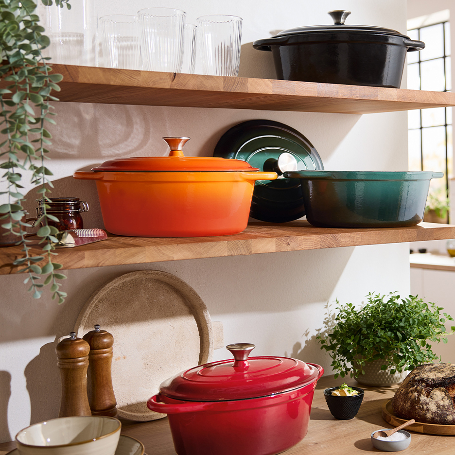 Casseroles en fonte colorées sur des étagères en bois dans une cuisine lumineuse.