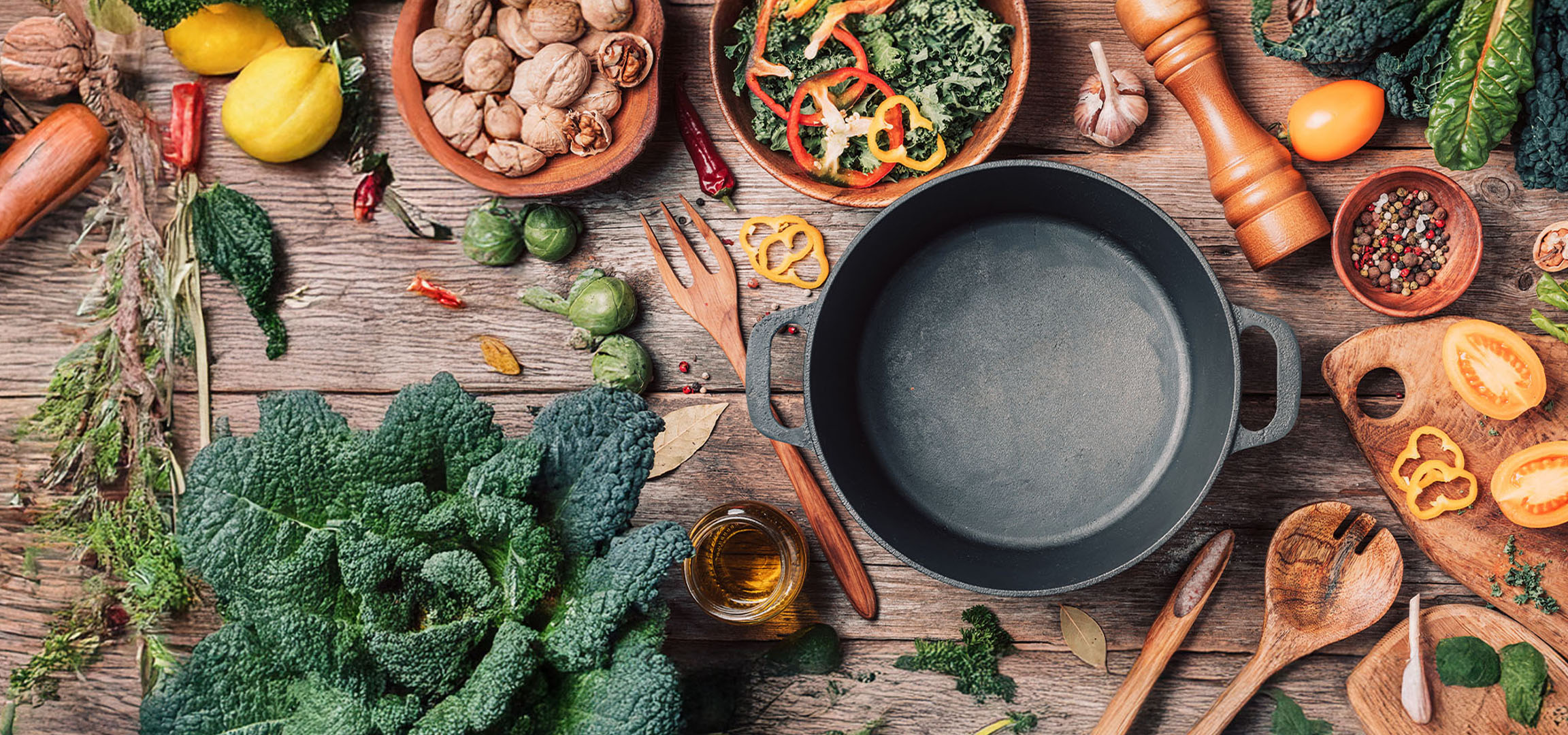 Une poêle en fonte entourée de légumes frais, de noix et d'épices sur une table en bois.