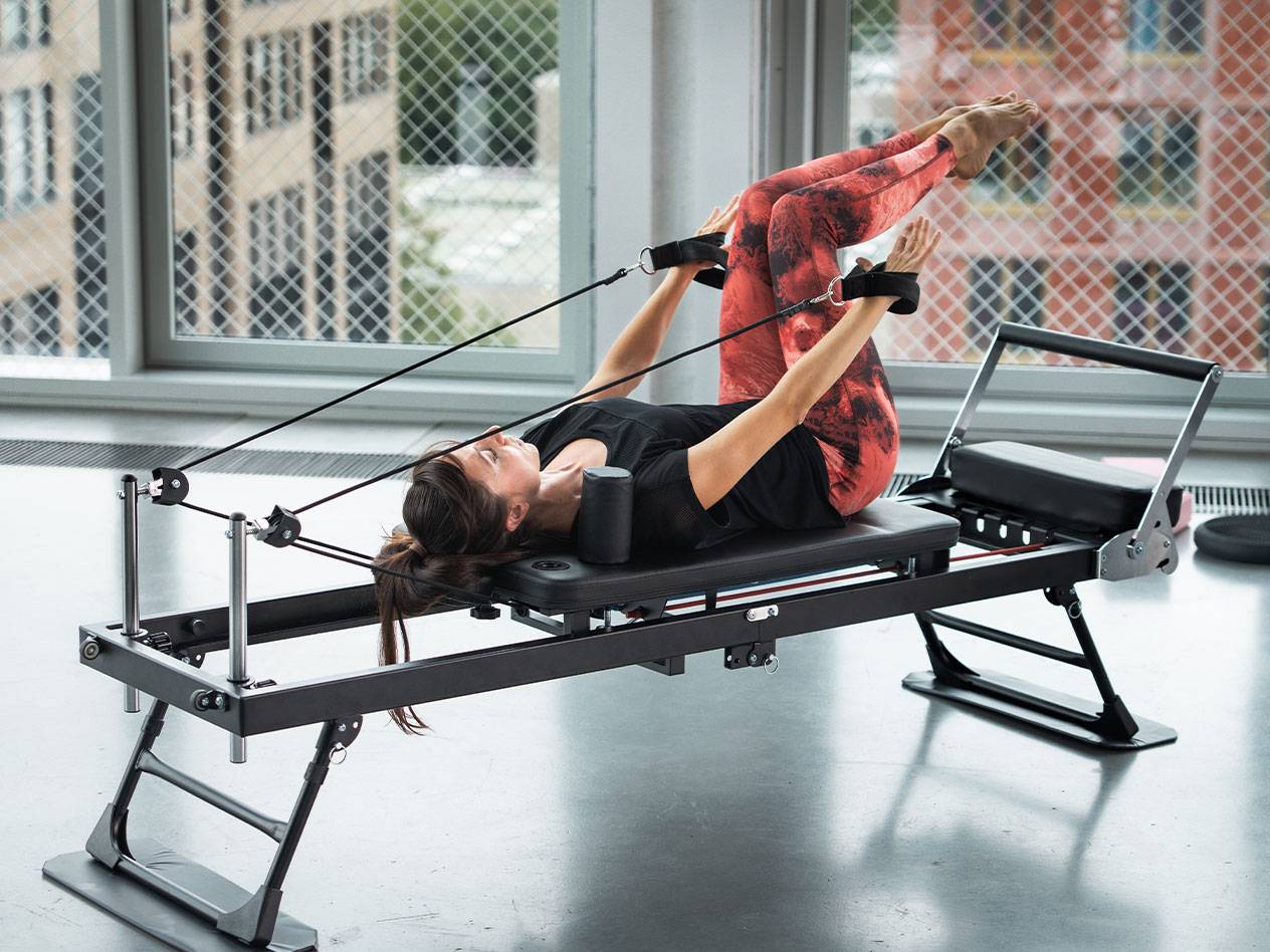 Femme faisant du Pilates sur un reformer avec un legging de yoga rouge.