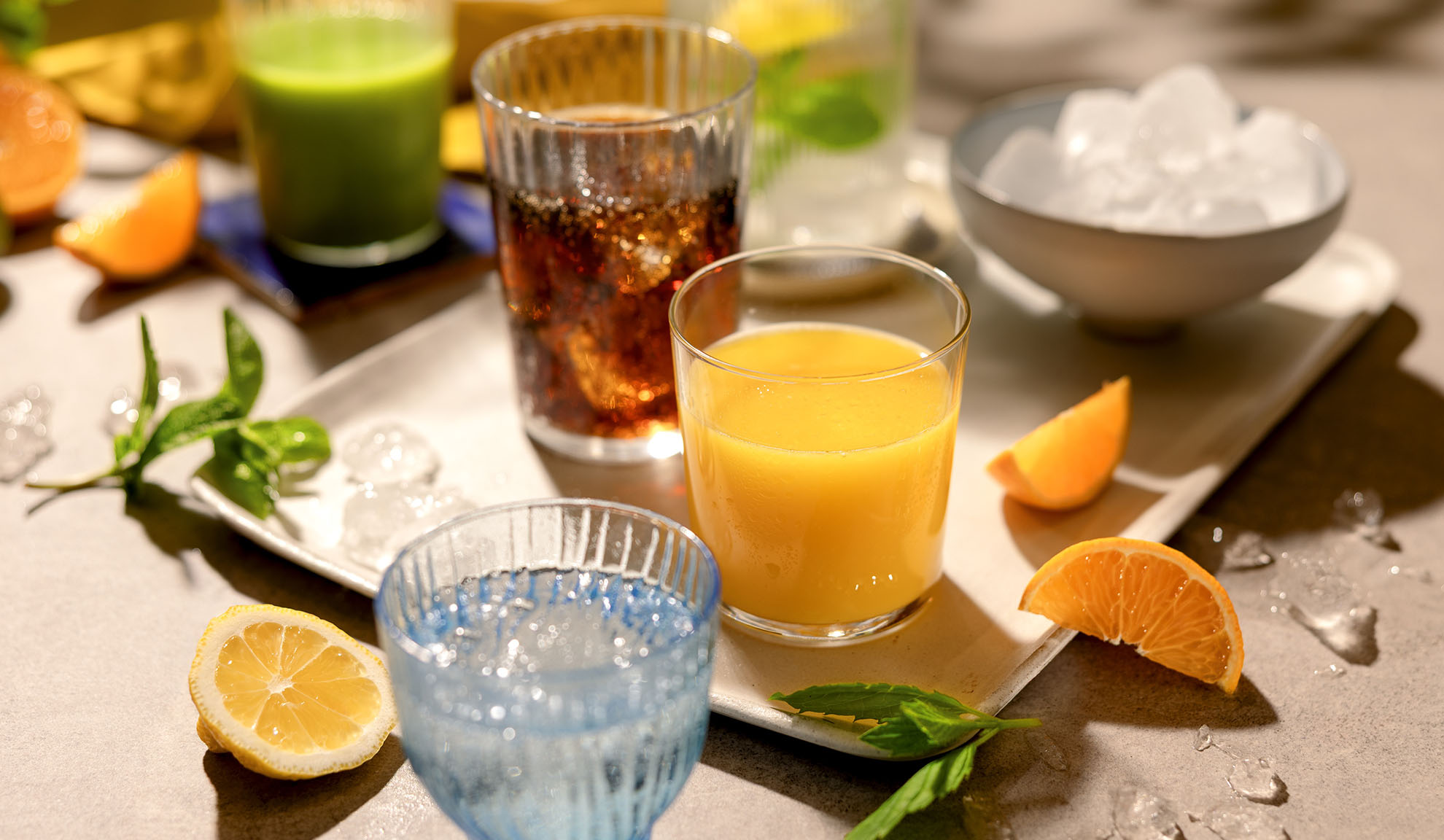 Diverses boissons rafraîchissantes avec de la glace, des tranches d'agrumes et de la menthe sur un plateau.