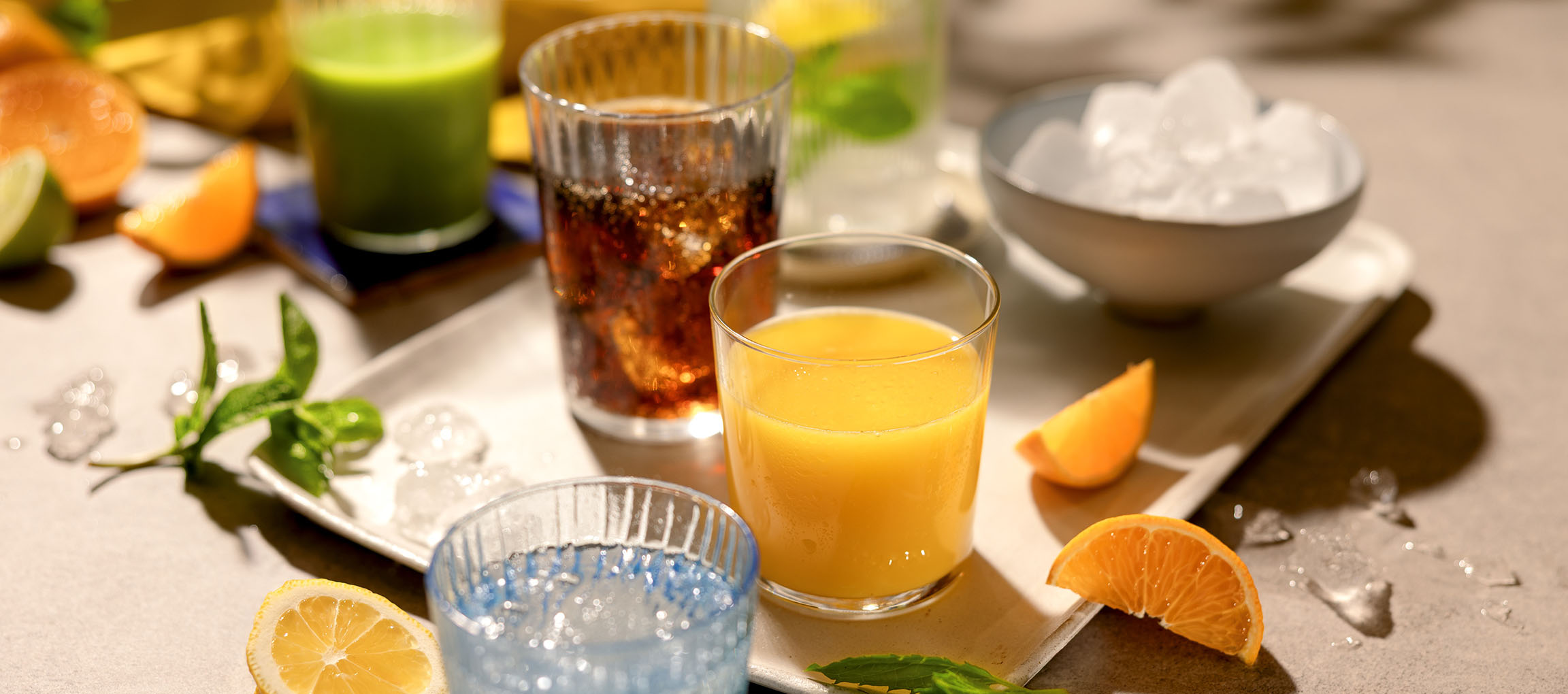 Diverses boissons rafraîchissantes et fruits sur un plateau, y compris du jus d'orange et des boissons gazeuses.
