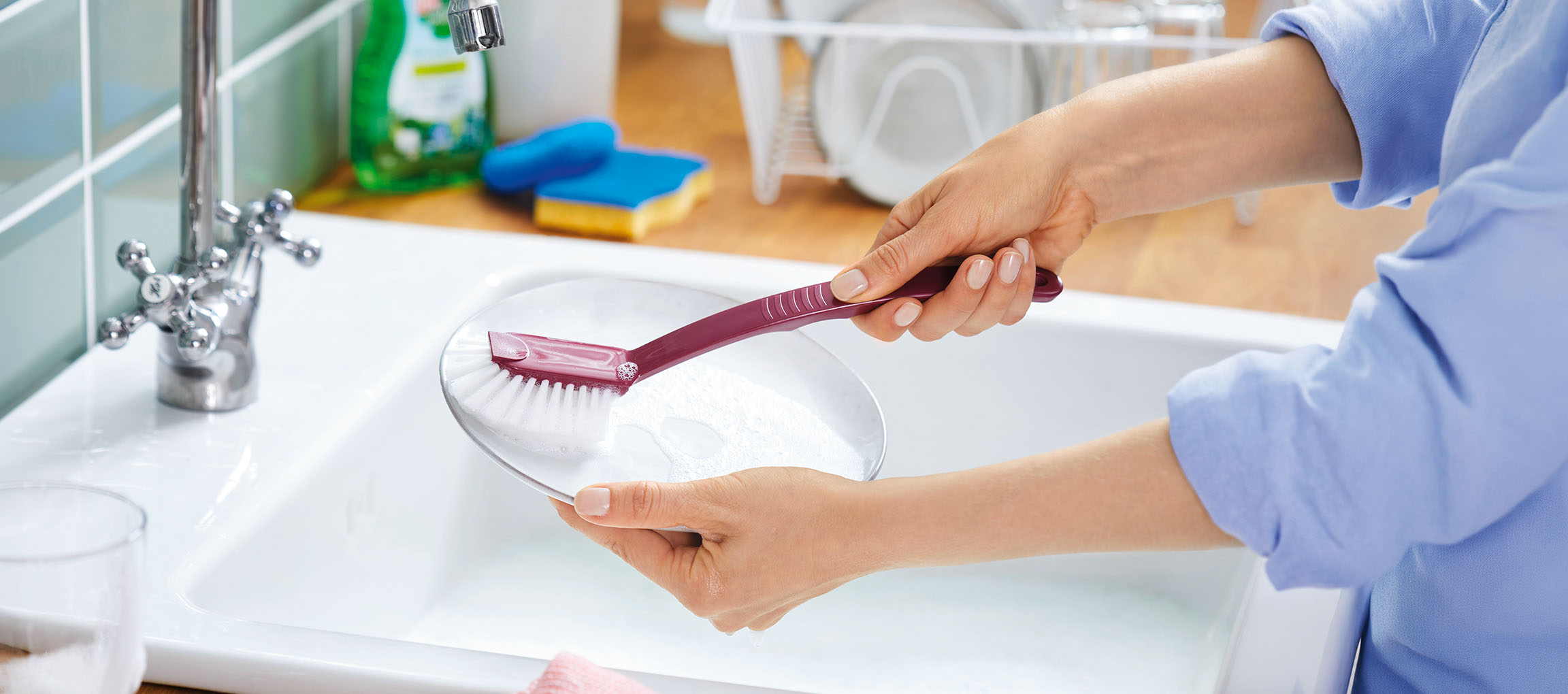 Femme faisant la vaisselle dans un évier avec une brosse et une assiette.