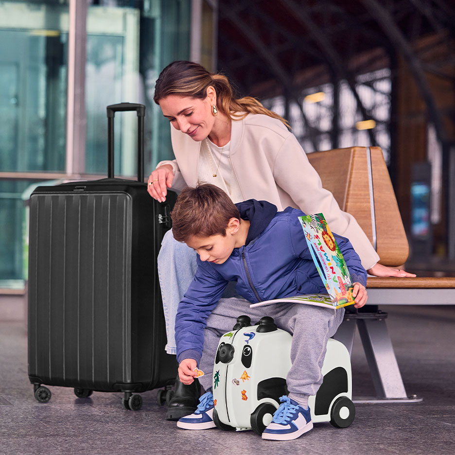 Femme et enfant avec une grande valise noire et une valise-trotteur panda à l'aéroport.