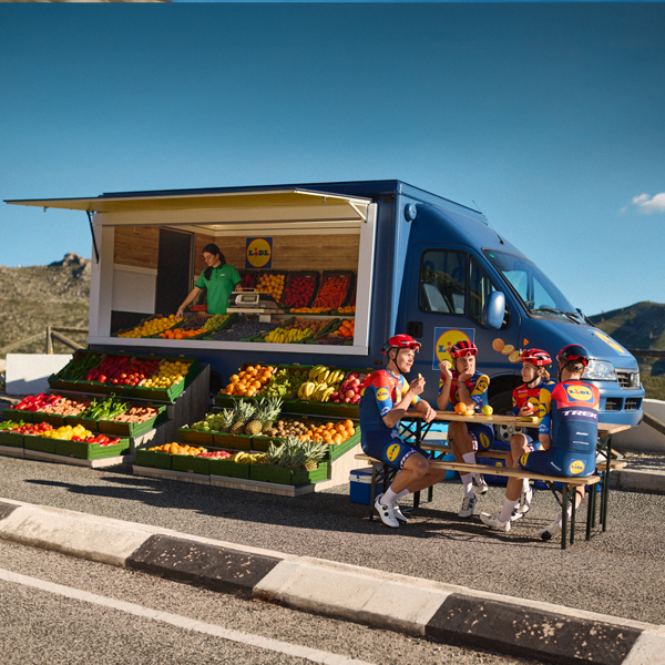 Des cyclistes font une pause près d'un camion Lidl rempli de fruits et légumes.
