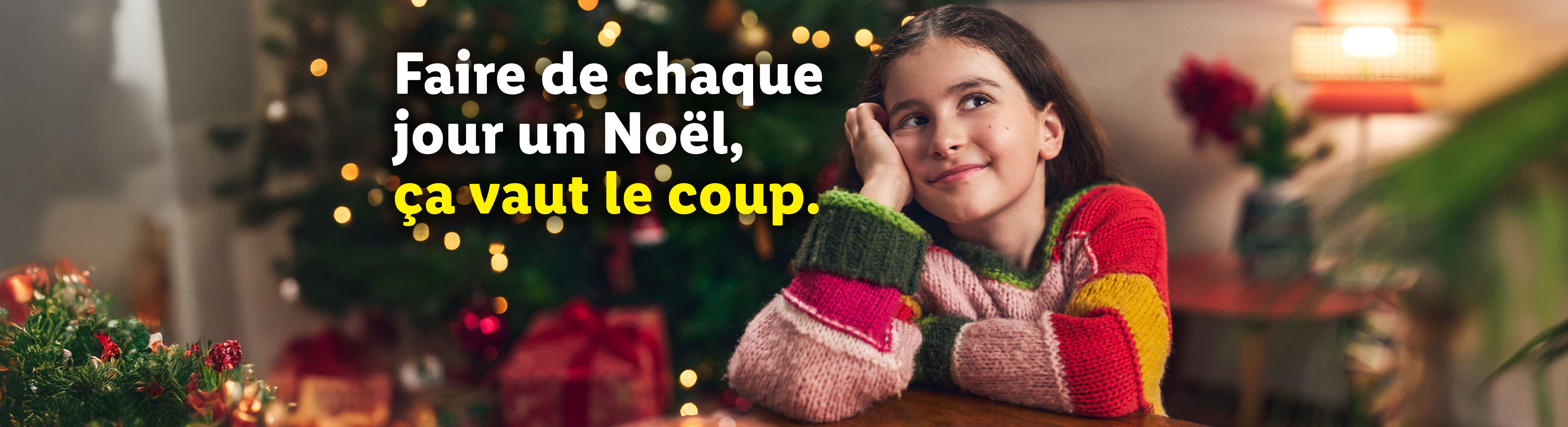 Une fille souriante devant un sapin de Noël, avec le texte : « Faire de chaque jour un Noël, ça vaut le coup. »