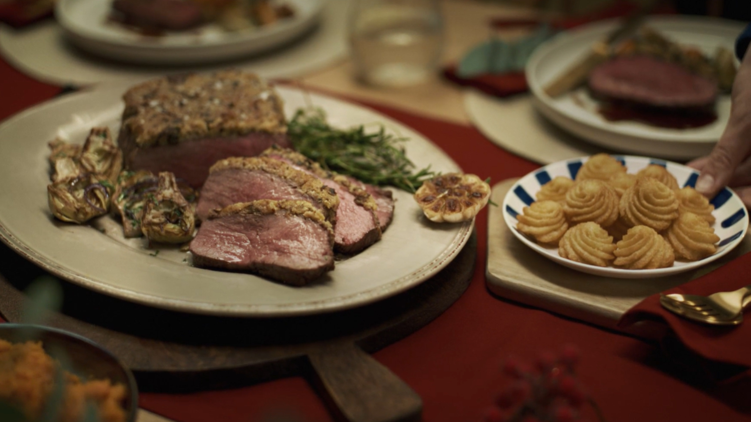 Un plat de rôti de bœuf tranché avec des artichauts et des pommes duchesse sur une table de fête.