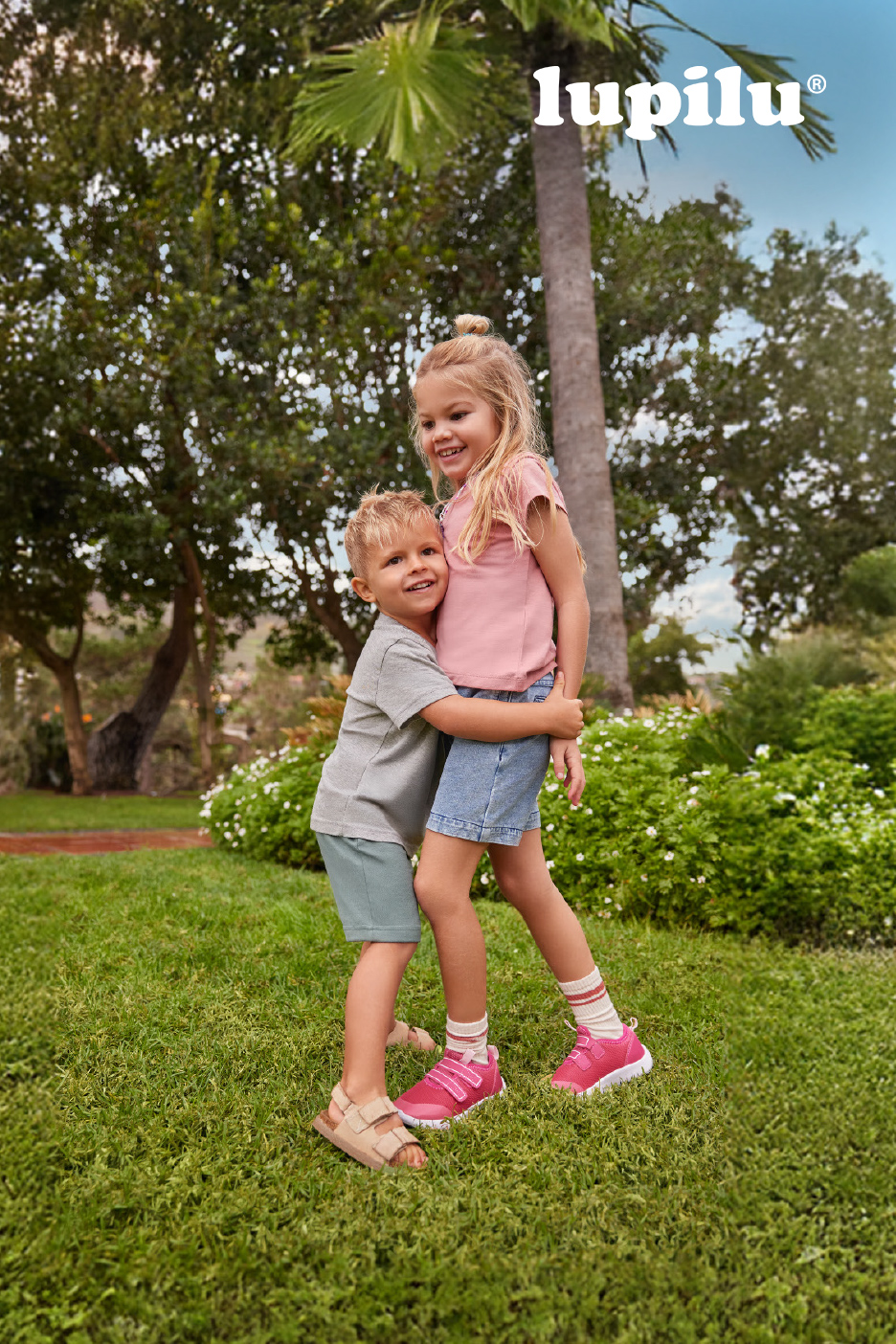 Deux enfants souriants, un garçon et une fille, s'étreignent dans un parc verdoyant.