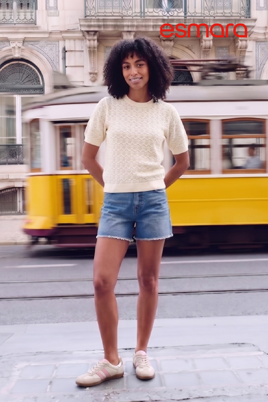 Femme en pull crème et short en jean, devant un tramway jaune en mouvement.