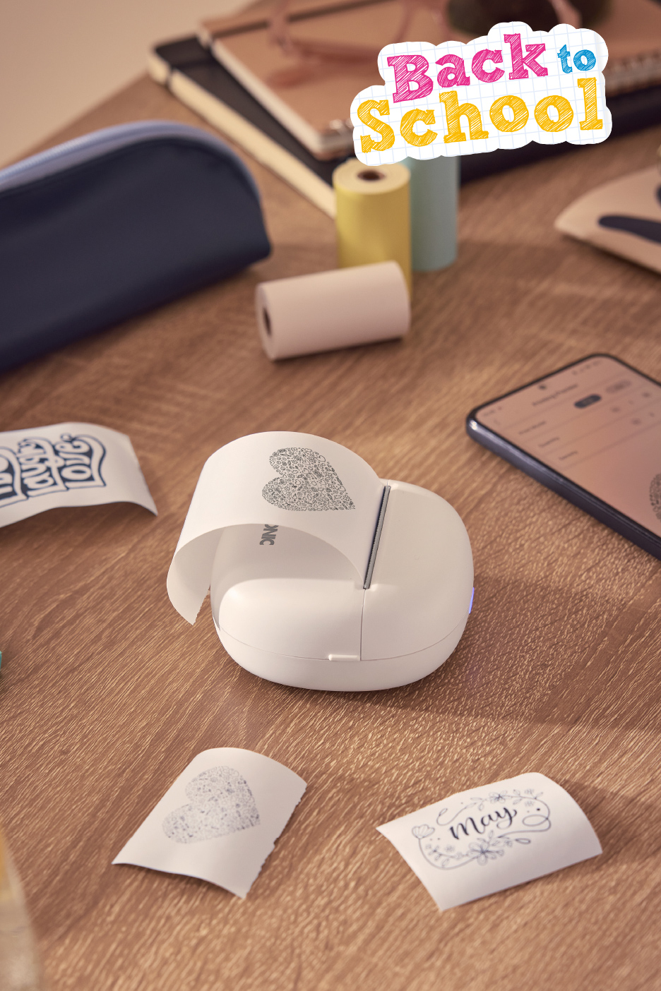 Imprimante portable blanche avec des rouleaux de papier et des impressions sur une table en bois, avec le texte 'Back to School'.