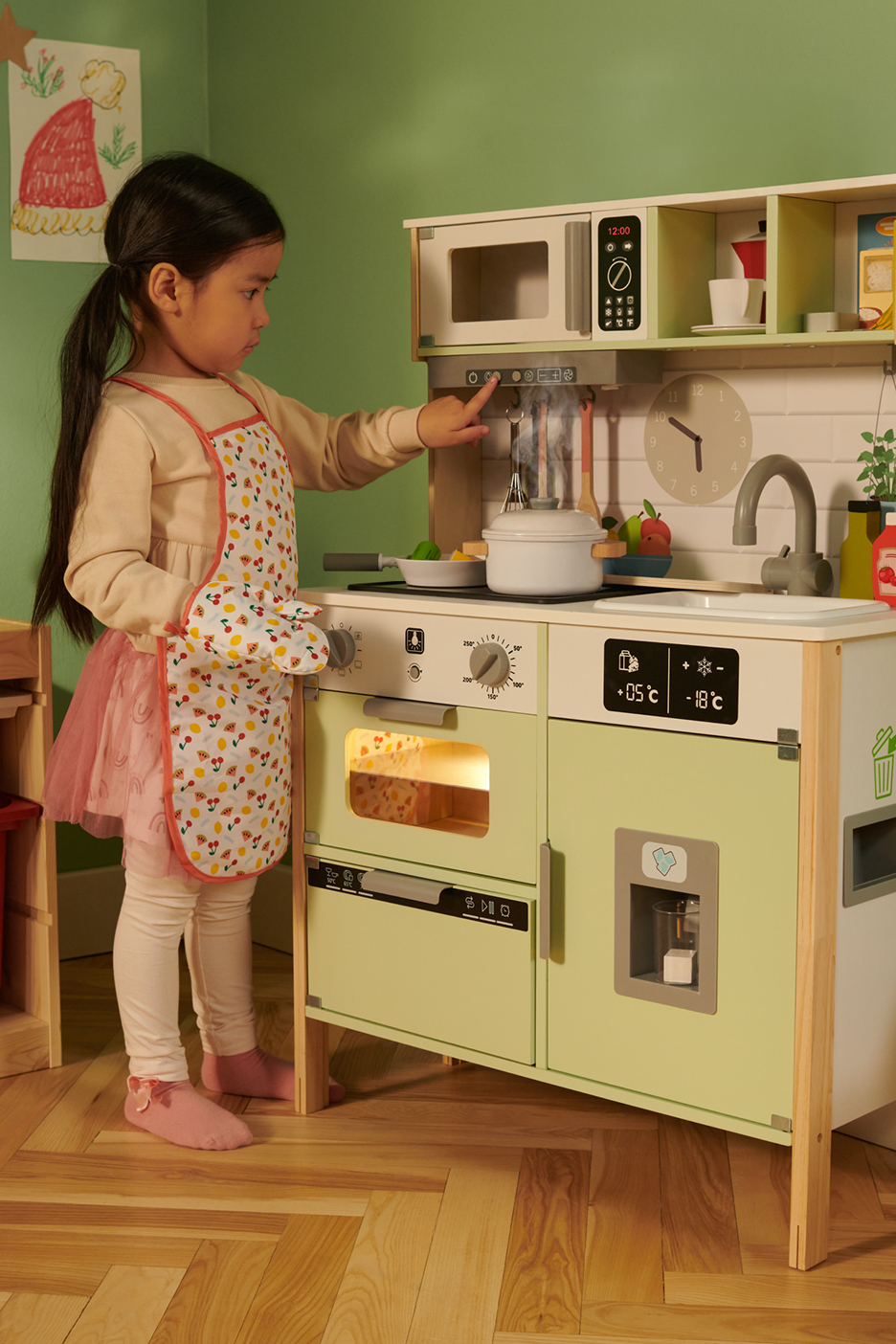 Une petite fille joue avec une cuisine pour enfants en bois.