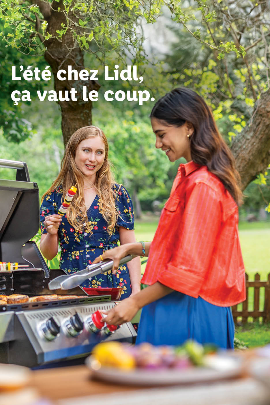 Deux femmes souriantes font un barbecue avec des brochettes et de la viande. Texte: L'été, ça vaut le coup.