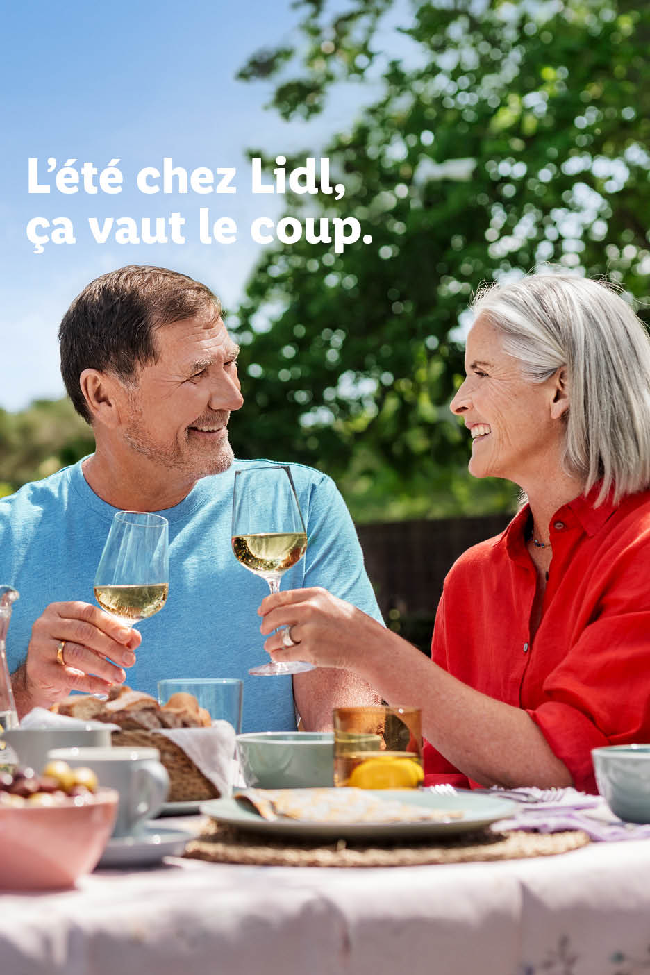 Un couple souriant trinque avec du vin blanc à une table d'été. Texte: L'été chez Lidl, ça vaut le coup.