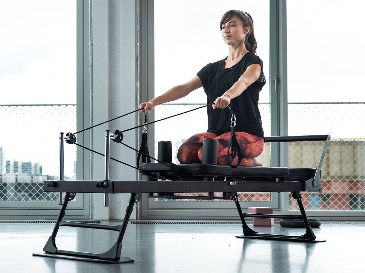 Femme faisant du Pilates sur un reformer avec de grandes fenêtres en arrière-plan.