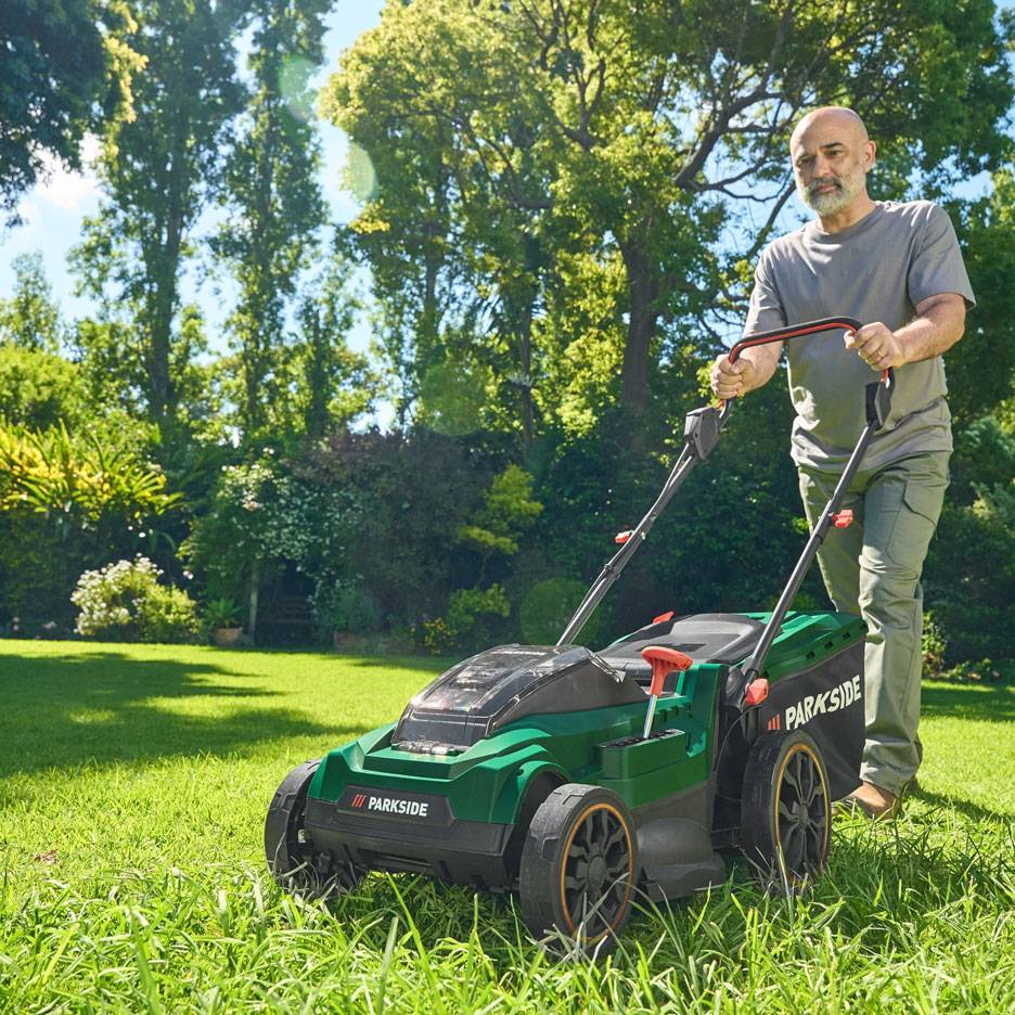 Homme tondant la pelouse avec une tondeuse verte dans un jardin ensoleillé.