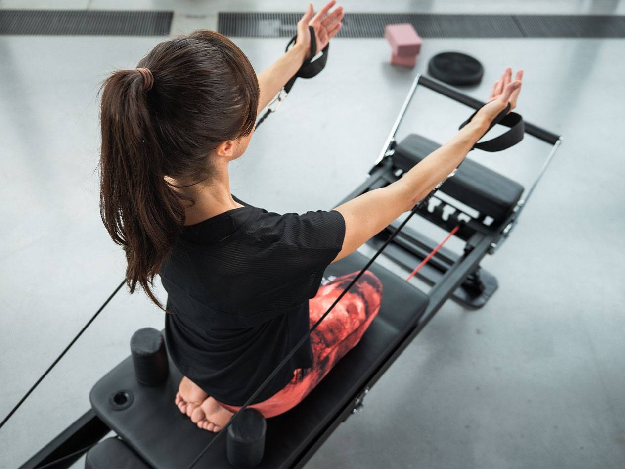Femme faisant du Pilates sur un appareil reformer avec des bandes de résistance.