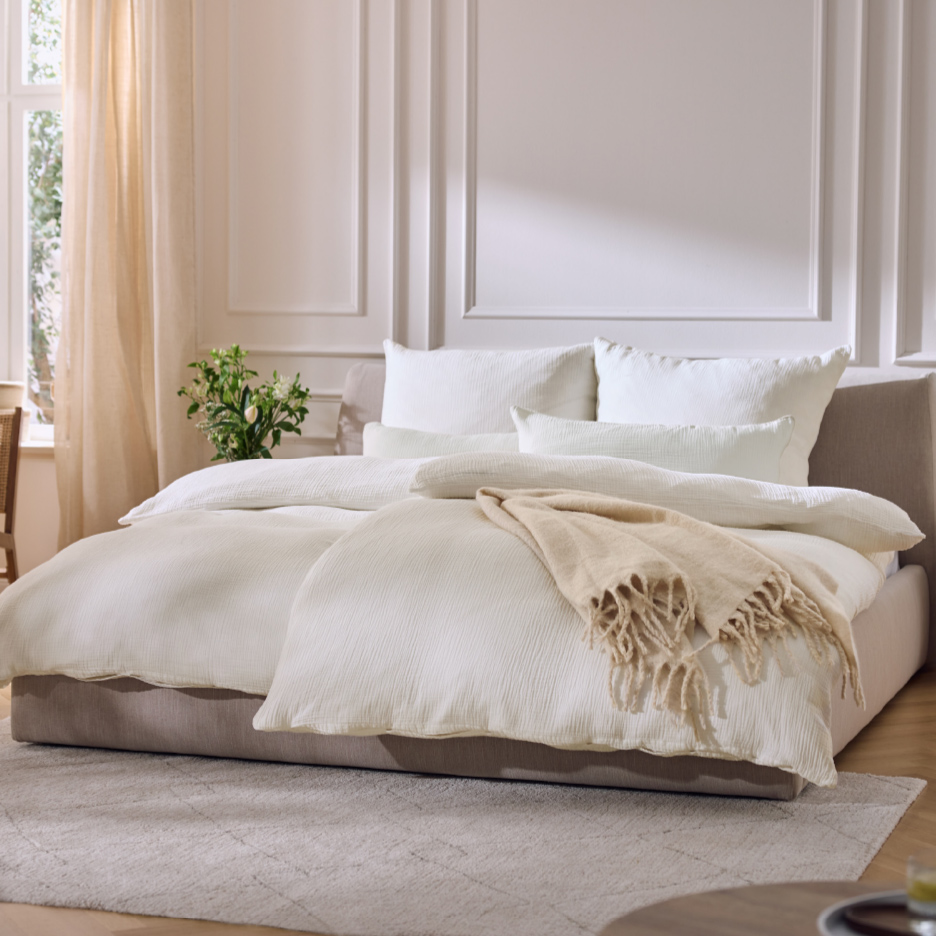 Chambre à coucher lumineuse avec un lit double beige, une literie blanche et un plaid beige.