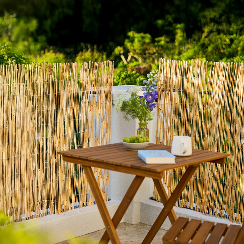 Un paravent en bambou sur un balcon avec une table en bois, des fleurs et des fruits.