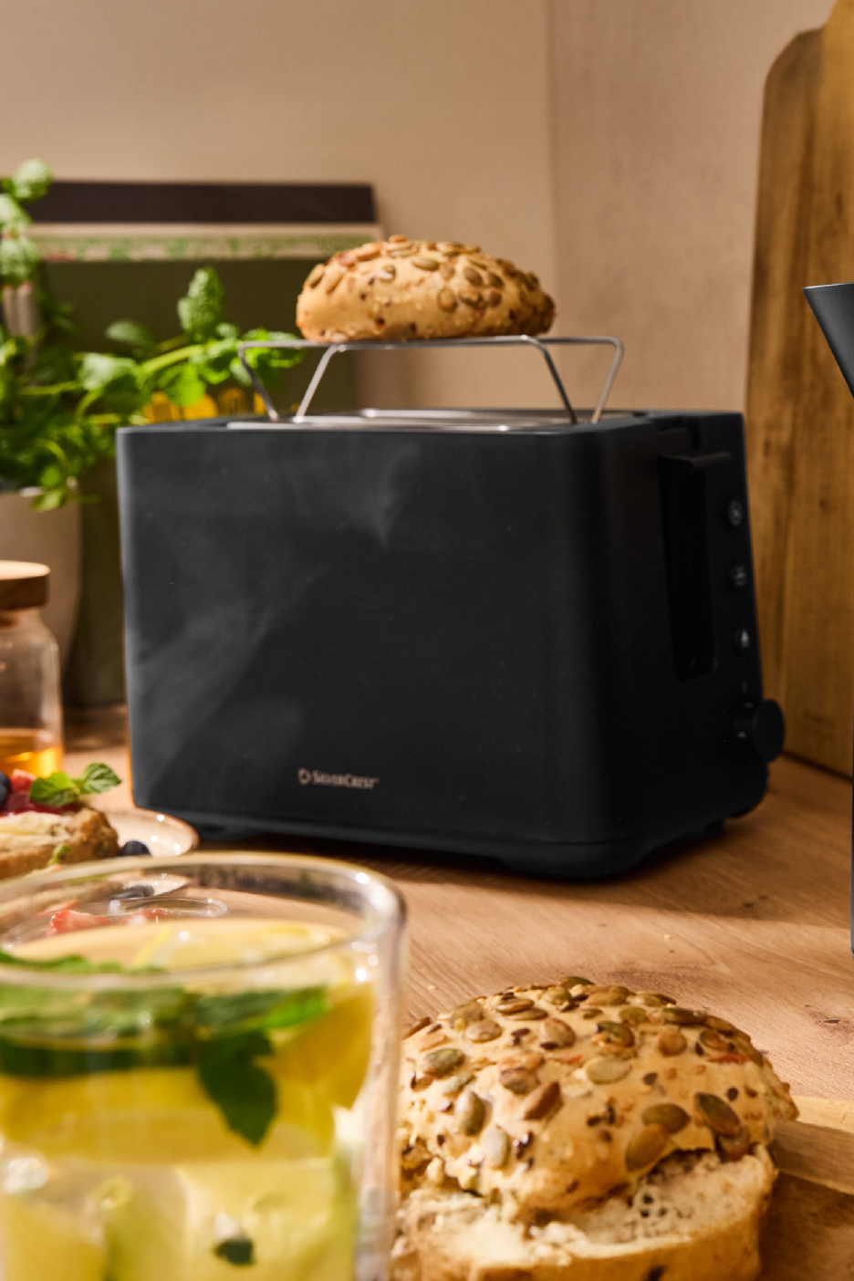 Grille-pain noir SilverCrest avec un petit pain aux graines sur le dessus, sur une table en bois.