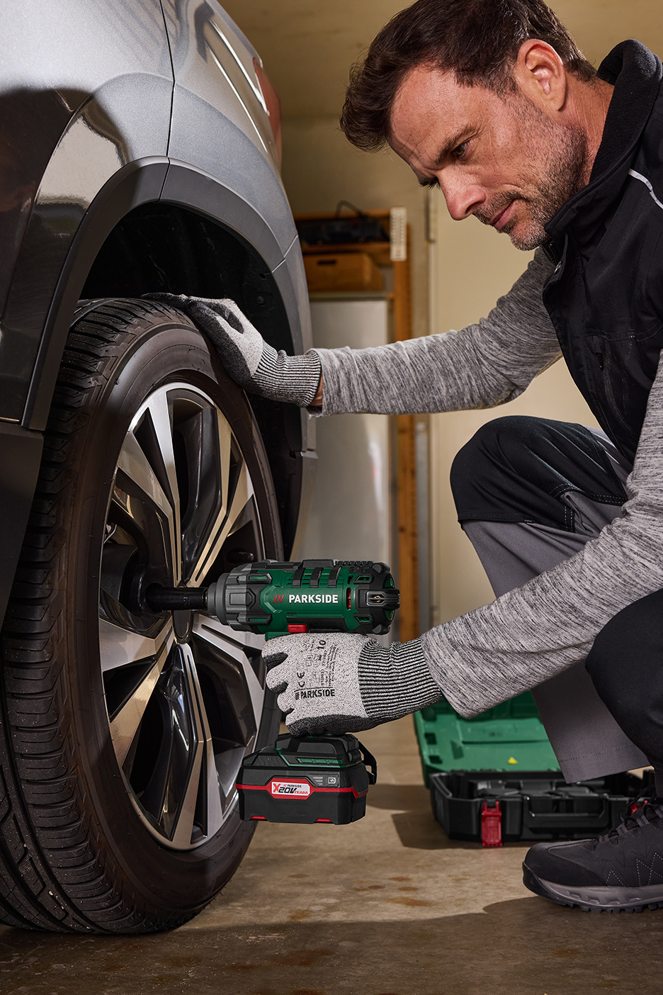 Un homme utilise une clé à chocs sans fil Parkside pour changer un pneu de voiture.