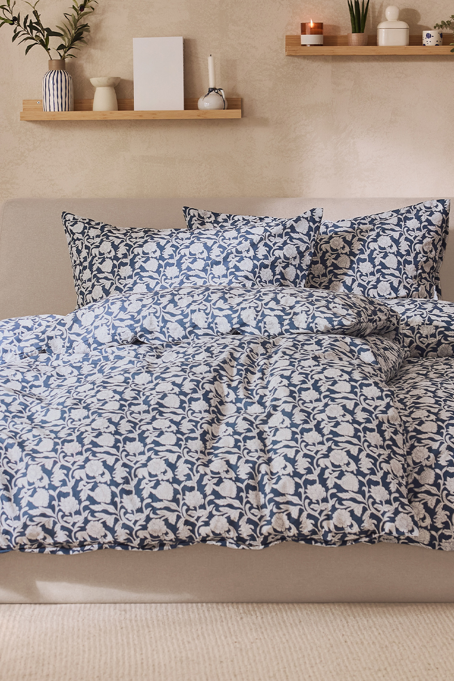 Literie à motifs floraux bleus et blancs sur un lit, avec des étagères en bois décorées au-dessus.