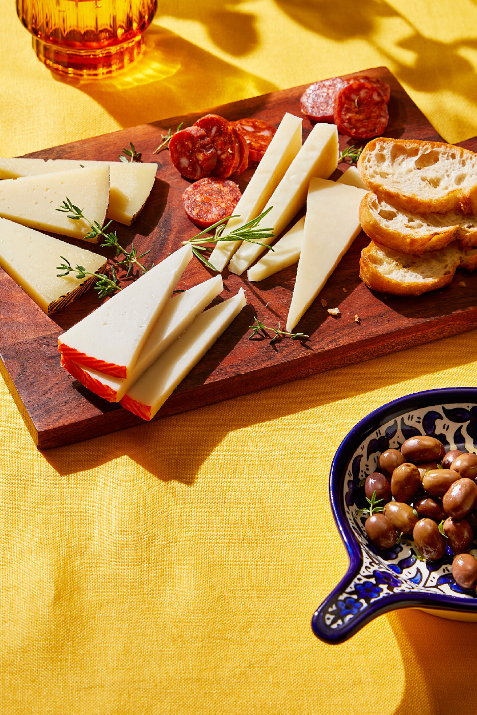 Un plateau de fromages et de charcuteries avec des olives et du pain sur une nappe jaune.