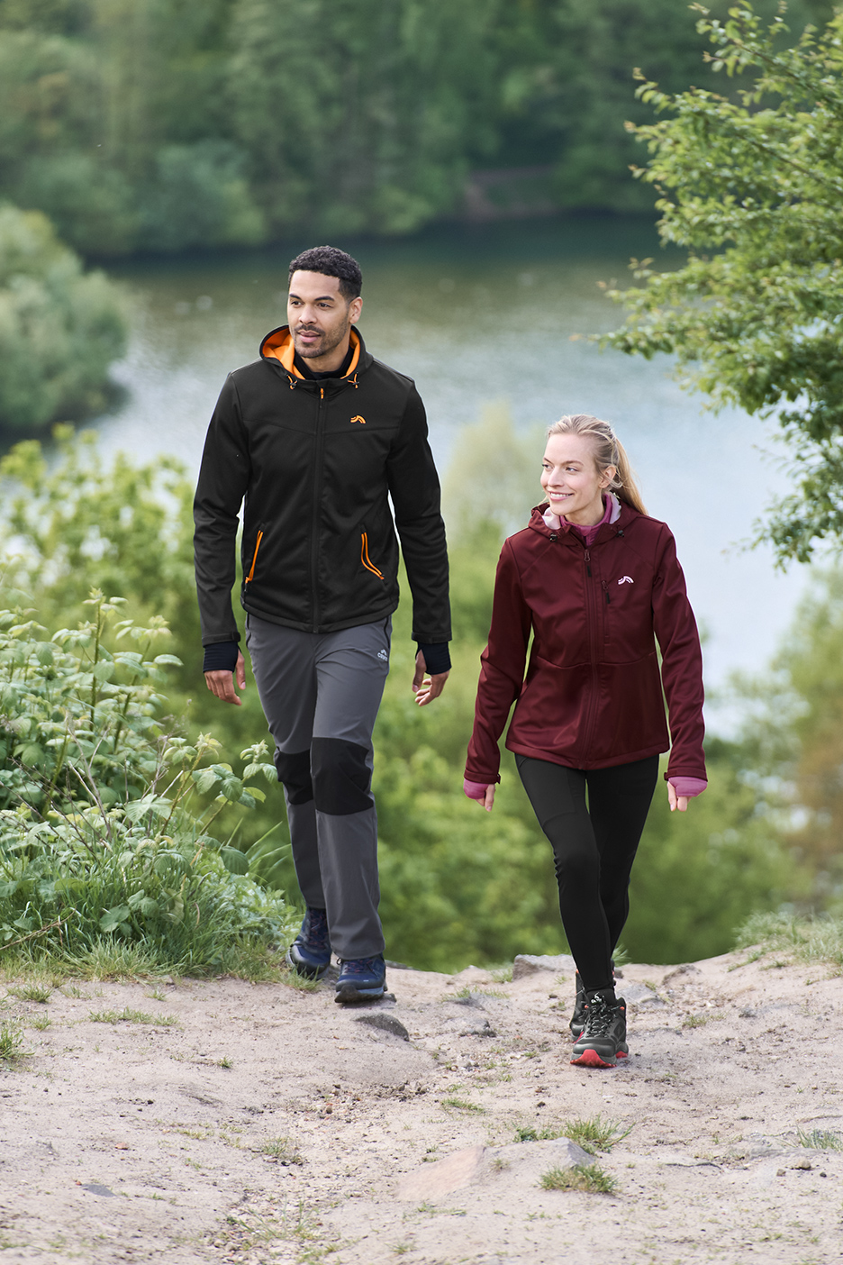 Deux personnes en vestes softshell et pantalons de randonnée marchent sur un sentier.