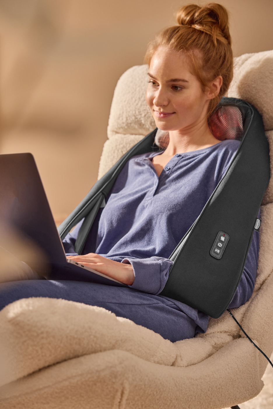 Femme utilisant un masseur de nuque et d'épaules tout en travaillant sur un ordinateur portable.