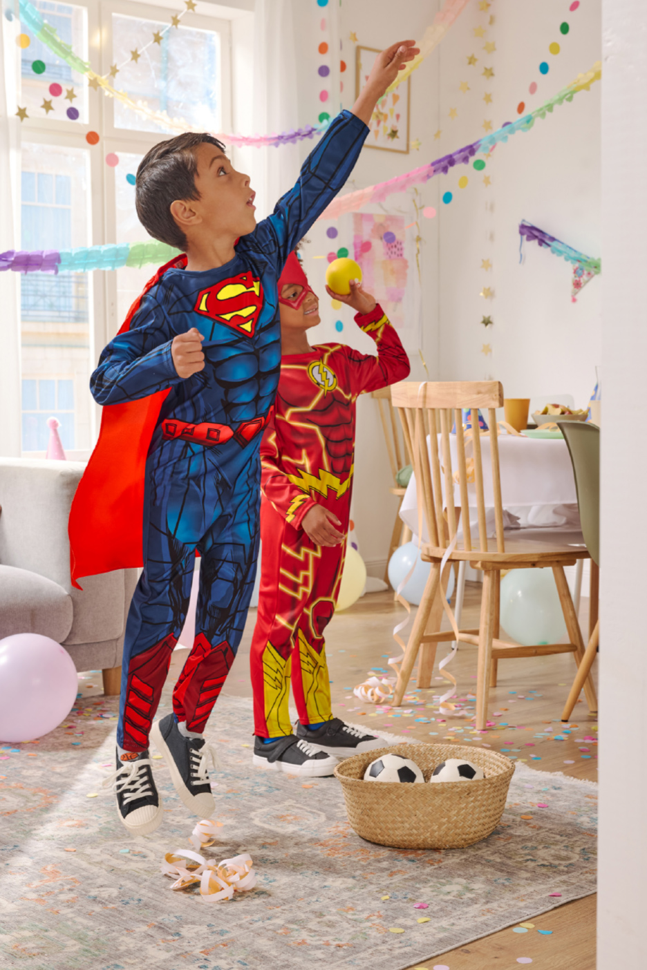 Deux enfants déguisés en super-héros jouent lors d'une fête d'anniversaire colorée.