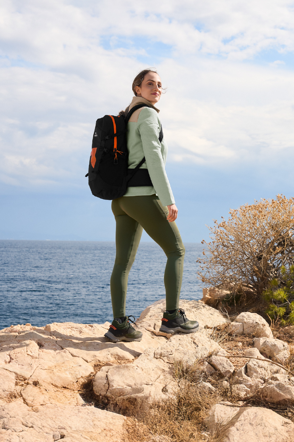 Femme en tenue de randonnée avec sac à dos et chaussures de marche, regardant l'océan.