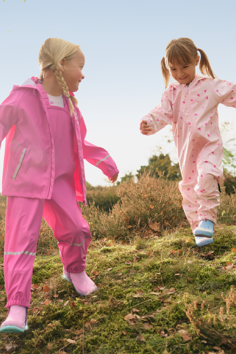 Deux enfants en cirés roses jouent dans la nature.