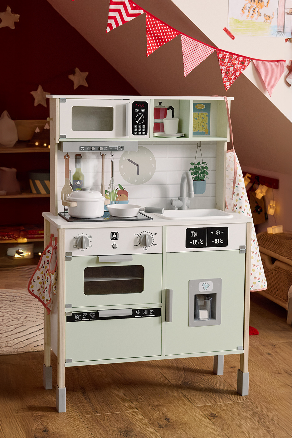 Cuisine de jeu en bois pour enfants avec accessoires, décorée de guirlandes.
