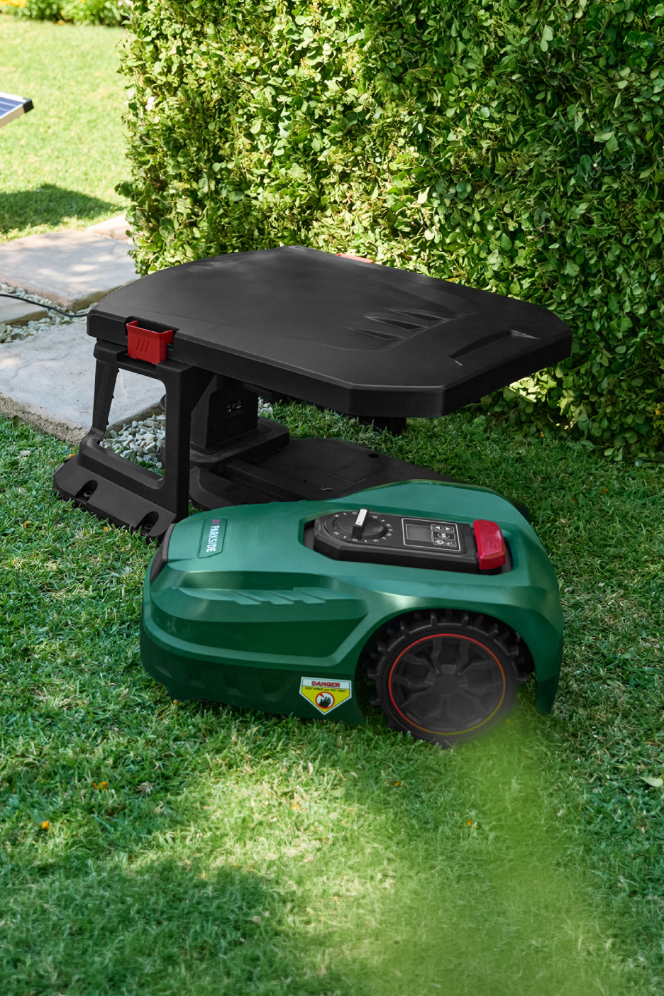 Tondeuse robot verte avec sa station de charge noire dans un jardin verdoyant.