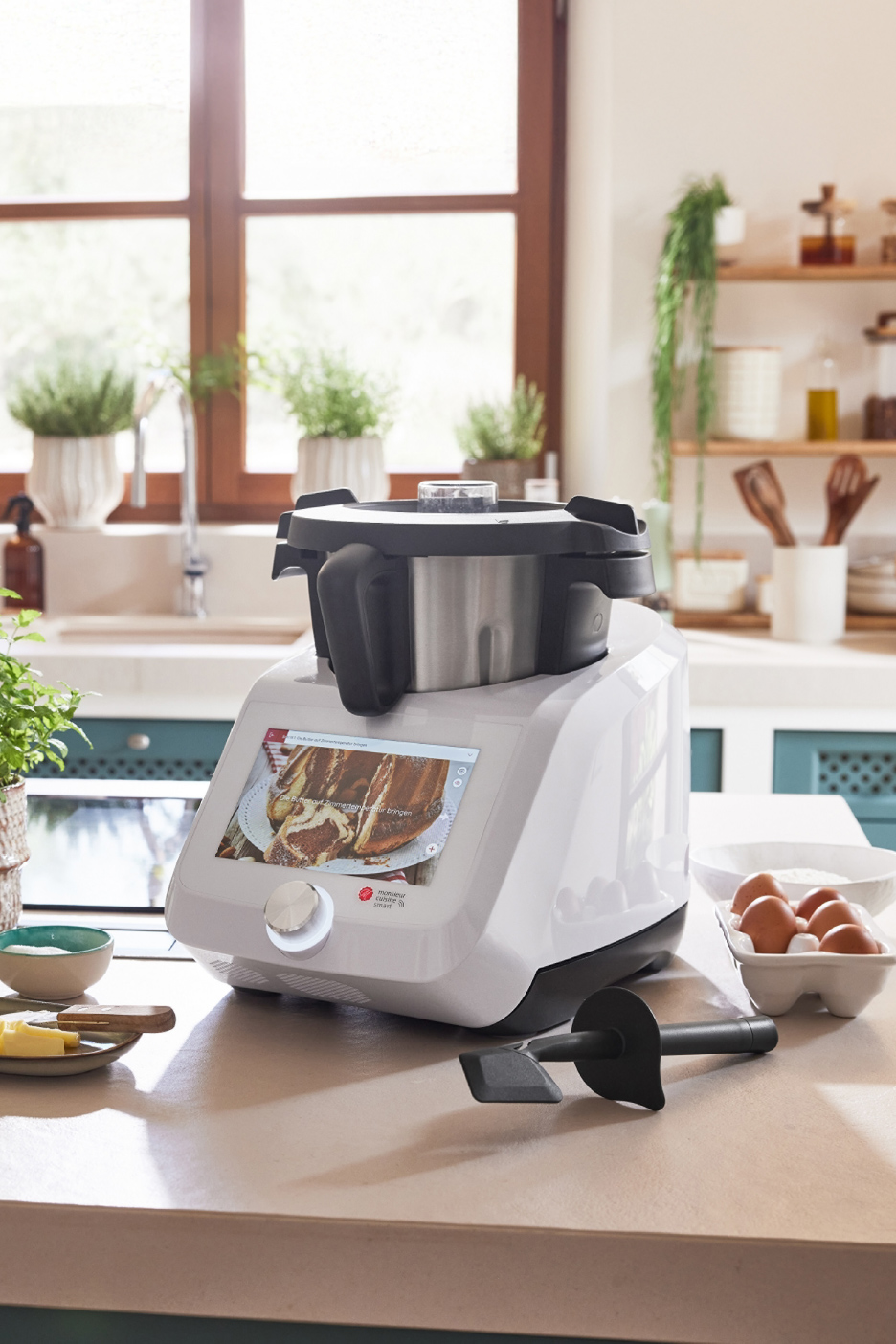 Robot de cuisine multifonction blanc avec écran affichant un gâteau, sur un comptoir de cuisine.