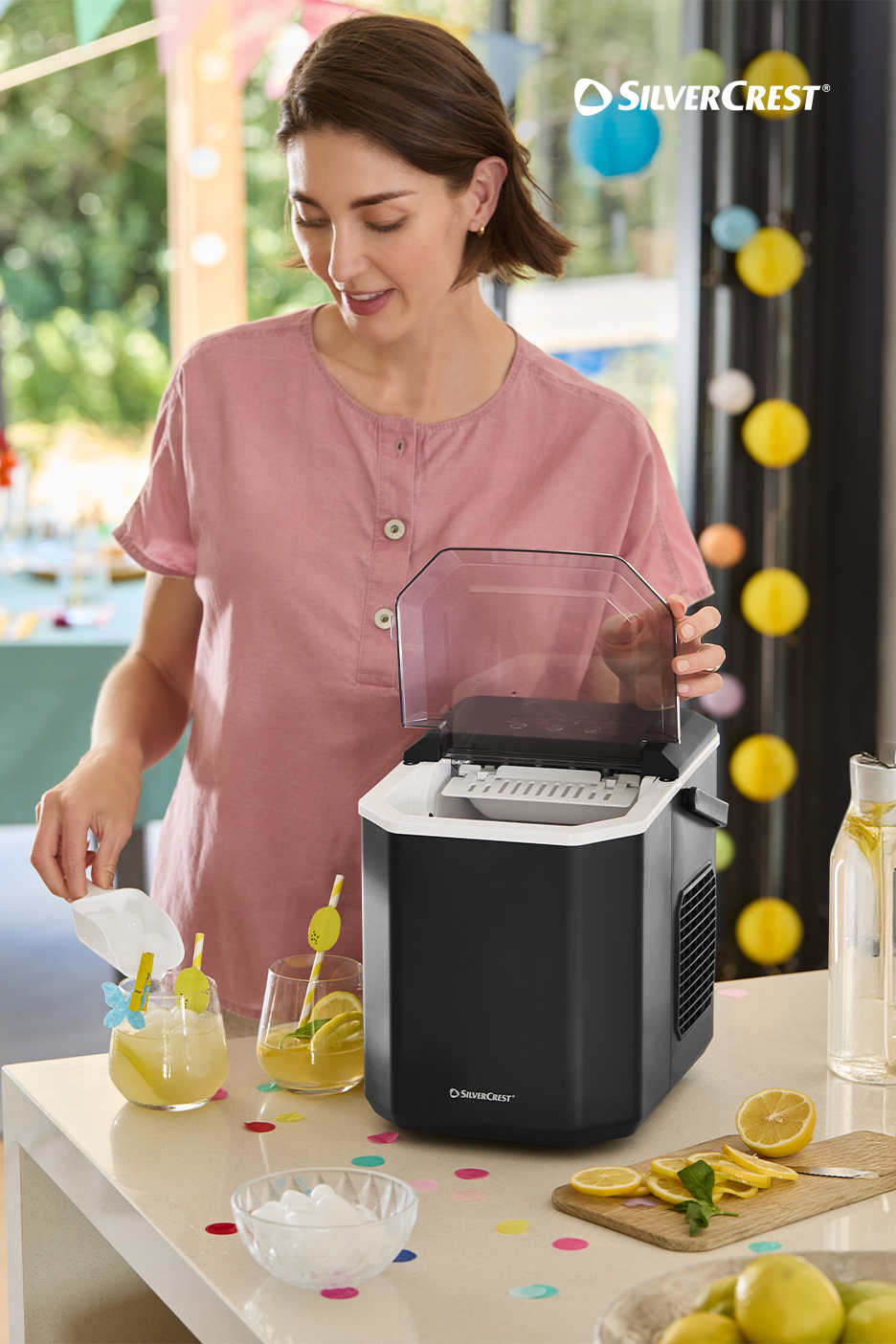 Une femme prépare des boissons avec une machine à glaçons, des citrons et des verres sur un comptoir.