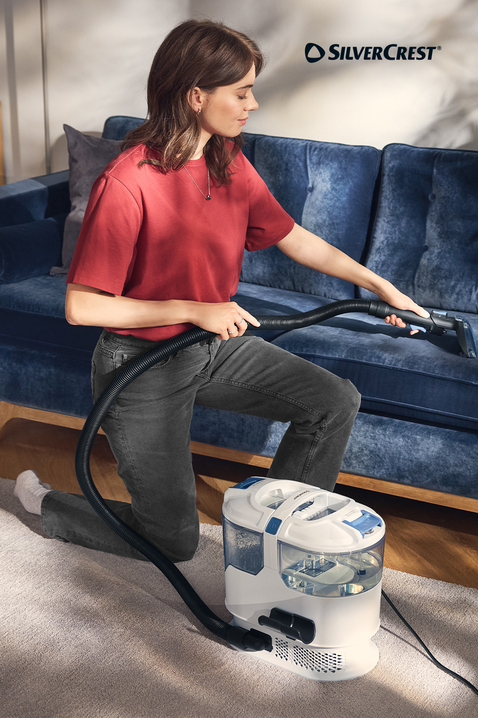 Femme nettoyant un canapé bleu avec un nettoyeur de tapis blanc et bleu.