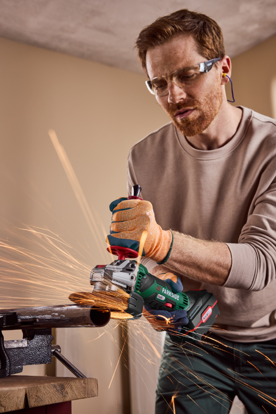 Homme utilisant une meuleuse d'angle sans fil pour couper un tuyau métallique, avec des étincelles.